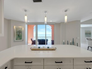 A modern kitchen with a large island, a sliding glass door to a balcony, and a view of the ocean.