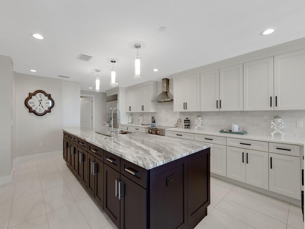 Una cocina moderna con armarios blancos, encimera de mármol e iluminación colgante.