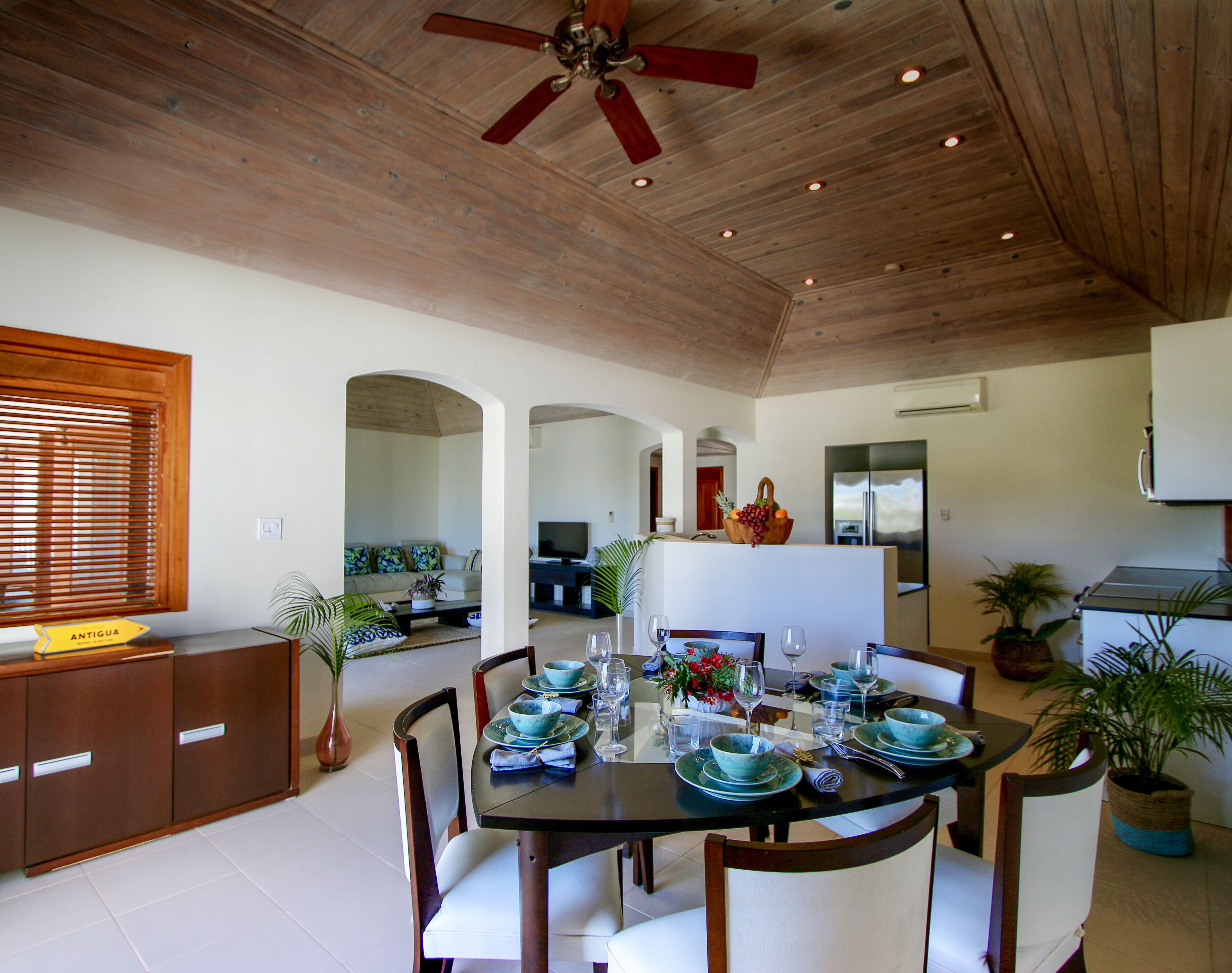Un comedor con techo de madera, una isla central con televisor, y una zona de cocina con refrigerador y estufa.