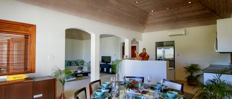 Un comedor con techo de madera, una isla central con televisor, y una zona de cocina con refrigerador y estufa.