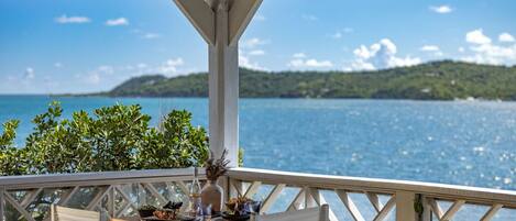 A wooden deck with a table set for dining, overlooking a body of water and green hills.