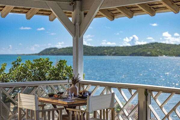 A wooden deck with a table set for dining, overlooking a body of water and green hills.