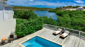 Une terrasse en bois avec une piscine, des chaises longues et une vue sur une étendue d’eau et la verdure.