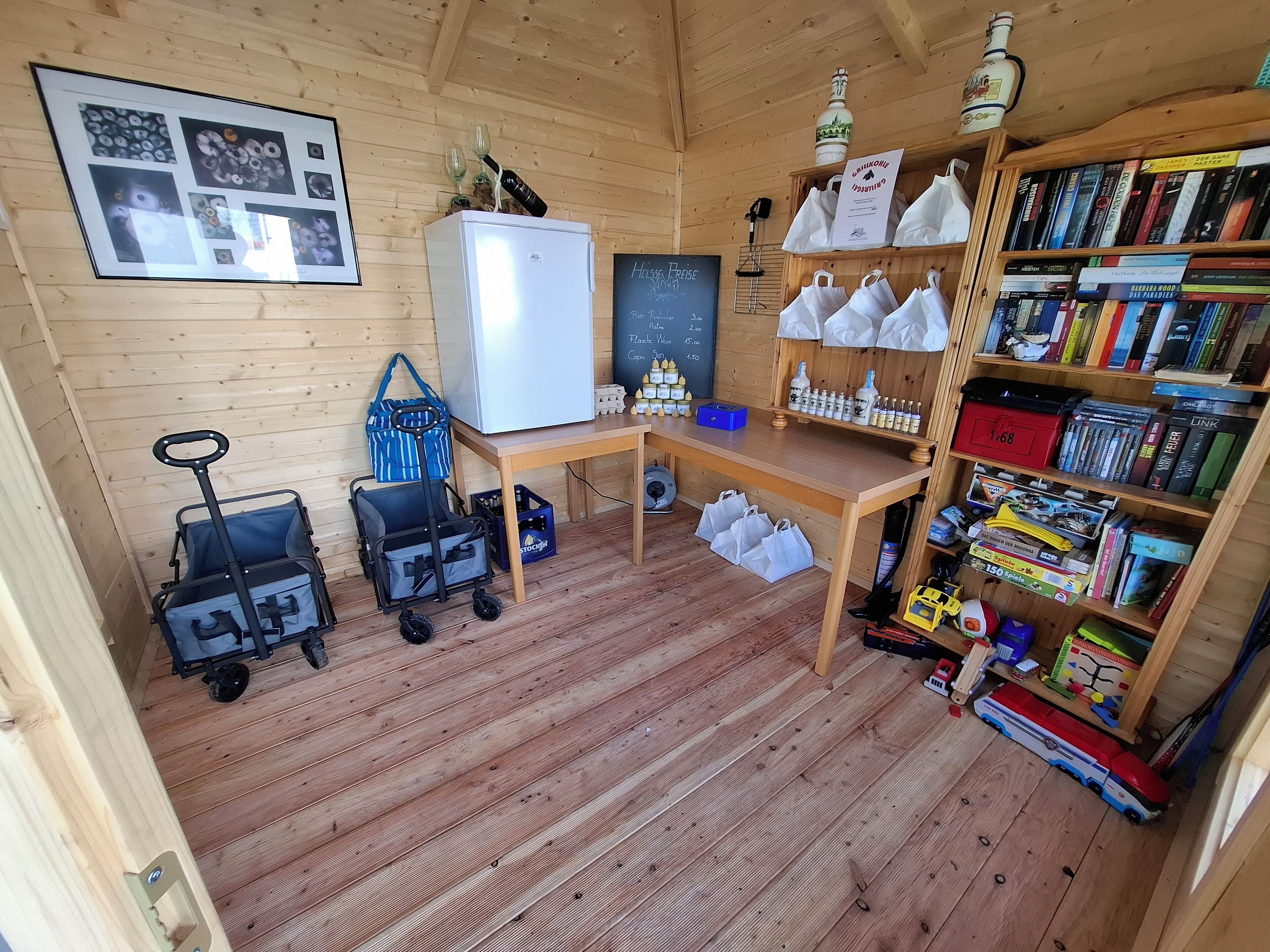 A cozy cabin interior with wooden walls, a refrigerator, a desk with a chalkboard, a bookshelf, and a stroller.