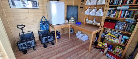A cozy cabin interior with wooden walls, a refrigerator, a desk with a chalkboard, a bookshelf, and a stroller.
