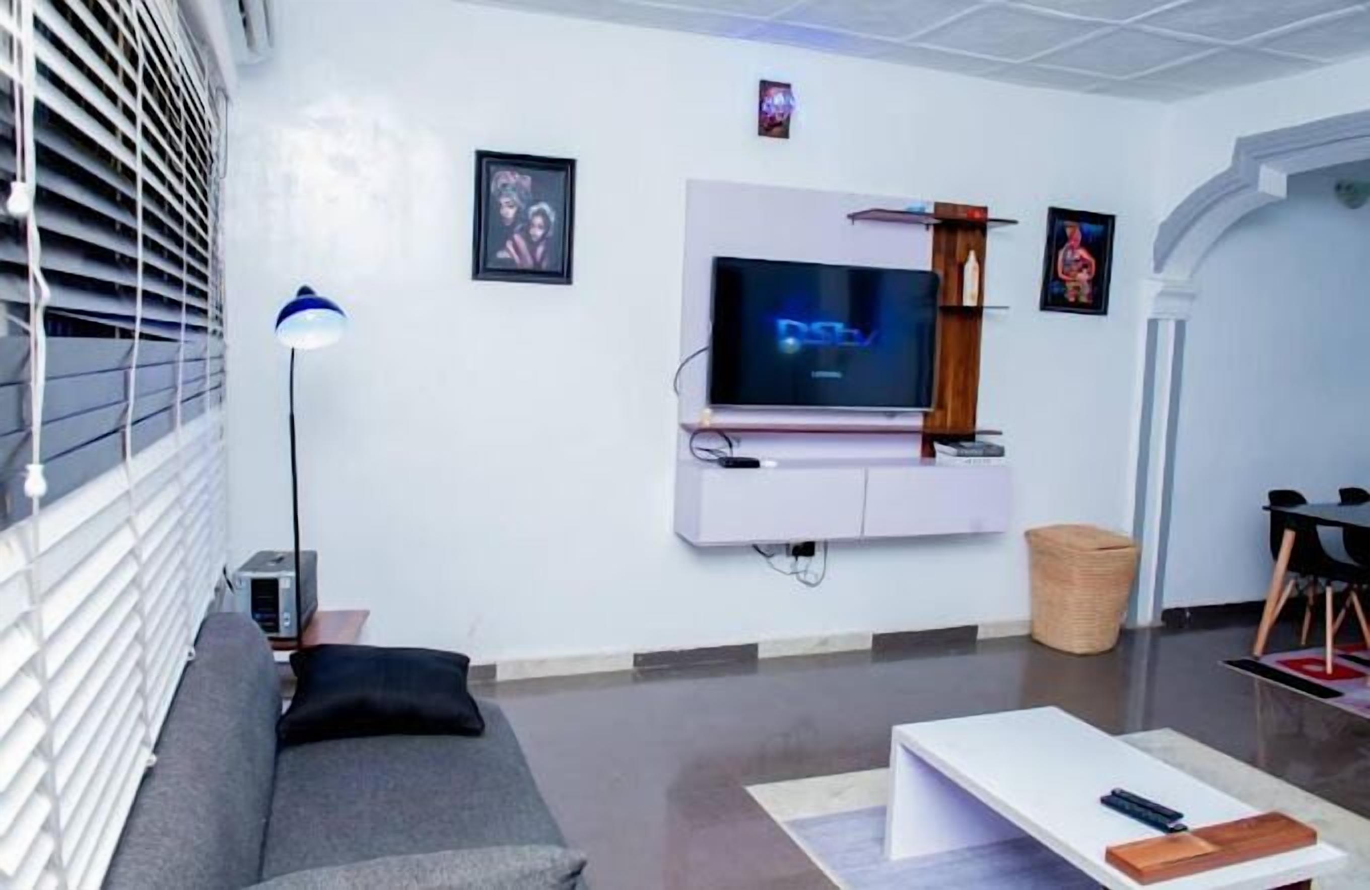 A modern living room with a flat-screen TV mounted on the wall, a grey sofa, a white coffee table, and a lamp.