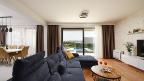 A modern living room with a sectional sofa, a dining area, and a large window with a view of the outdoors. - Villa Sunlight Zadar Villas (Zadar)
