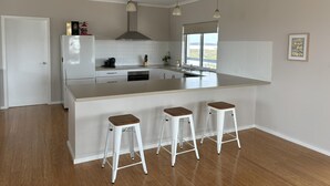 A modern kitchen with a large island, white cabinetry, and three bar stools.
