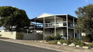 A two-story building with a covered balcony, a car parked in front, and a clear blue sky.