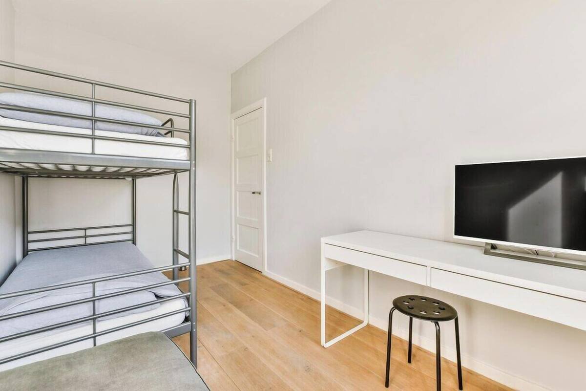 A bunk bed with a desk and a TV in a room with white walls and wooden flooring.