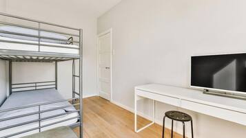 Una cama litera con escritorio y televisor en una habitación con paredes blancas y suelo de madera.