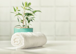 Une serviette blanche enroulée sur une surface blanche, avec une plante en pot en arrière-plan.