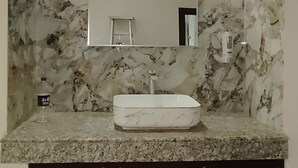 Un baño con salpicadero de mármol, un lavabo blanco y un mueble oscuro debajo.