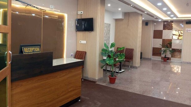 Un área de recepción con un mostrador de madera, un televisor de pantalla plana y un cartel de recepción. Se observan plantas en macetas y sillas acolchadas al fondo.