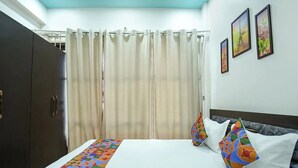 Una habitación de hotel con cama, cortinas, un armario y tres cuadros en la pared.