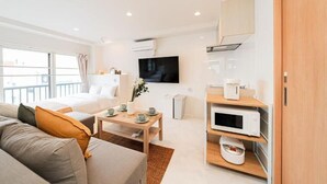 A modern hotel room with a sofa, a coffee table, a TV, a microwave, and a wooden cabinet. - SAIEI HOTEL (Tokyo)
