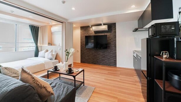 A modern hotel room with a large bed, a seating area with a coffee table, a TV mounted on a stone wall, and a kitchenette with a microwave. - SAIEI HOTEL (Tokyo)