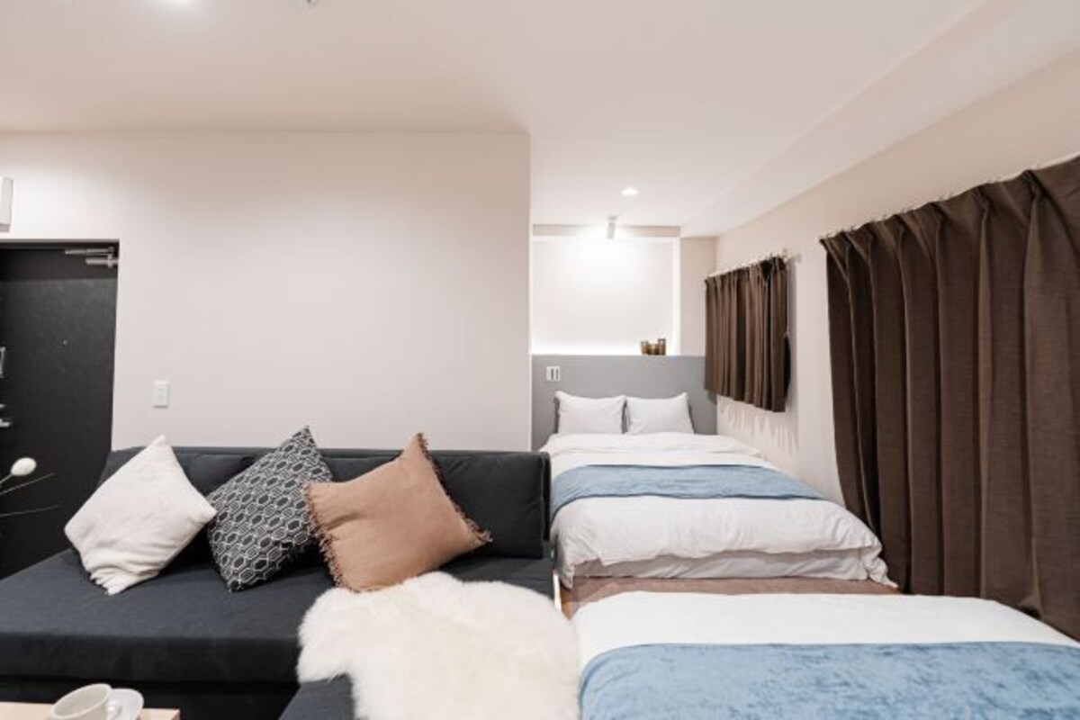 A hotel room with a sofa, two beds, and a large window with curtains.