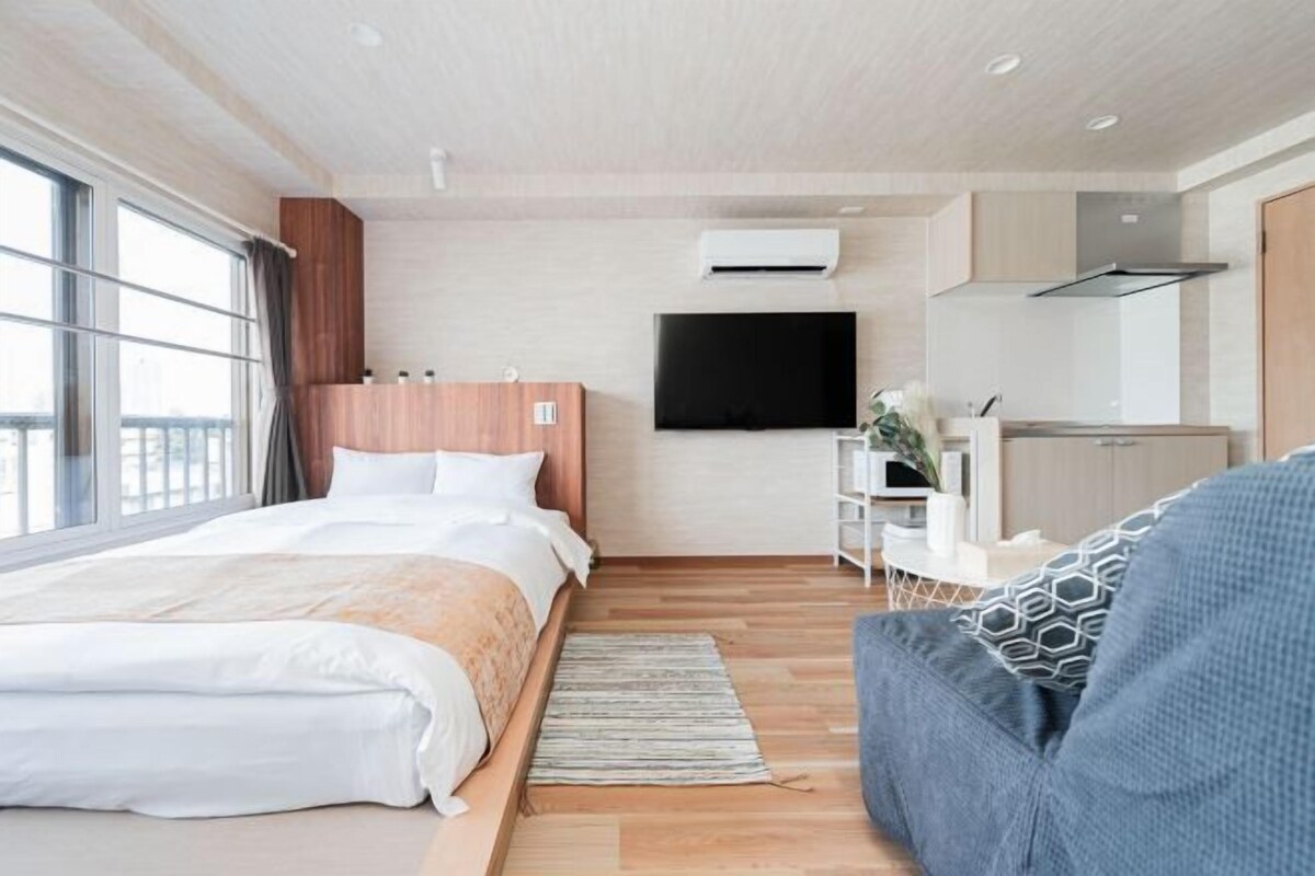 Un moderno cuarto de hotel con una cama grande, un televisor de pantalla plana, una kitchenette y vistas a través de la ventana.