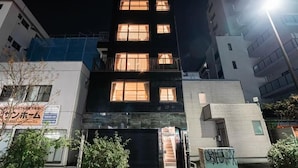 A multi-story building with illuminated windows at night, a visible storefront, and a gated entrance. - SAIEI HOTEL (Tokyo)