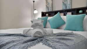 Un lit bien fait, avec une couverture grise, des coussins turquoise et une tête de lit dotée d’étagères.