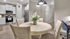 Une cuisine moderne avec des meubles blancs, un four à micro-ondes, une cuisinière et un réfrigérateur. On y trouve une table à manger avec des chaises et un vase de fleurs.