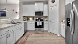 Une cuisine moderne avec des armoires blanches, des appareils en acier inoxydable et un plancher en bois.