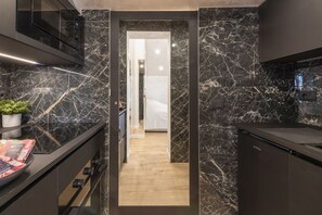 A modern kitchen with dark marble countertops, a built-in oven, and a wooden floor leading to a hallway.