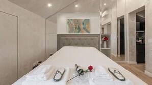 A modern hotel room with a large bed, a tufted headboard, a painting on the wall, and a small shelf with a vase of flowers. - GARIBALDI, 64 – In the heart of the historic center (Milano)