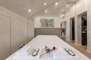 A modern hotel room with a large bed, a tufted headboard, a painting on the wall, and a small shelf with a vase of flowers. - GARIBALDI, 64 – In the heart of the historic center (Milano)