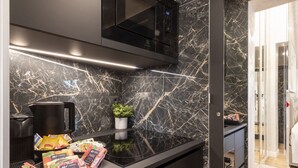 A modern kitchen with a black countertop, a coffee maker, a small potted plant, and various food items.