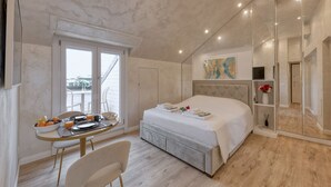 A bedroom with a bed, a dining table with breakfast, a large window, and a mirror.