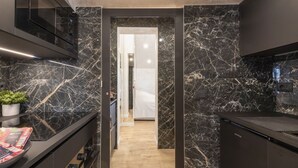 A modern kitchen with dark marble countertops, a built-in oven, and a wooden floor leading to a hallway. - GARIBALDI, 64 – In the heart of the historic center (Milano)