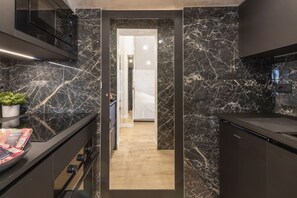 A modern kitchen with dark marble countertops, a built-in oven, and a wooden floor leading to a hallway. - GARIBALDI, 64 – In the heart of the historic center (Milano)