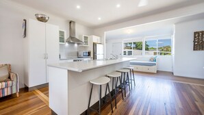 A modern kitchen with a central island, bar stools, and a view of the outdoors. - 65 Ocean Roads, Brooms Head (Brooms Head)
