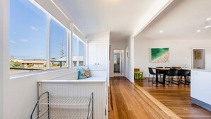 A modern kitchen with a view of the outside, a dining area with a beach-themed painting, and a hallway leading to another room. - 65 Ocean Roads, Brooms Head (Brooms Head)