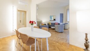 A dining area with a white table and wicker chairs, a sofa set with cushions, and a radiator.