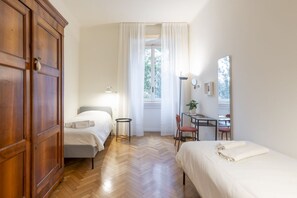 A bedroom with two beds, a desk, a chair, a wardrobe, and a window with curtains.