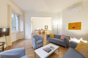 A modern living room with a sofa, armchair, and coffee table. There is a dining area in the background with a table and chairs.