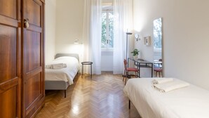 A bedroom with two beds, a desk, a chair, a wardrobe, and a window with curtains.