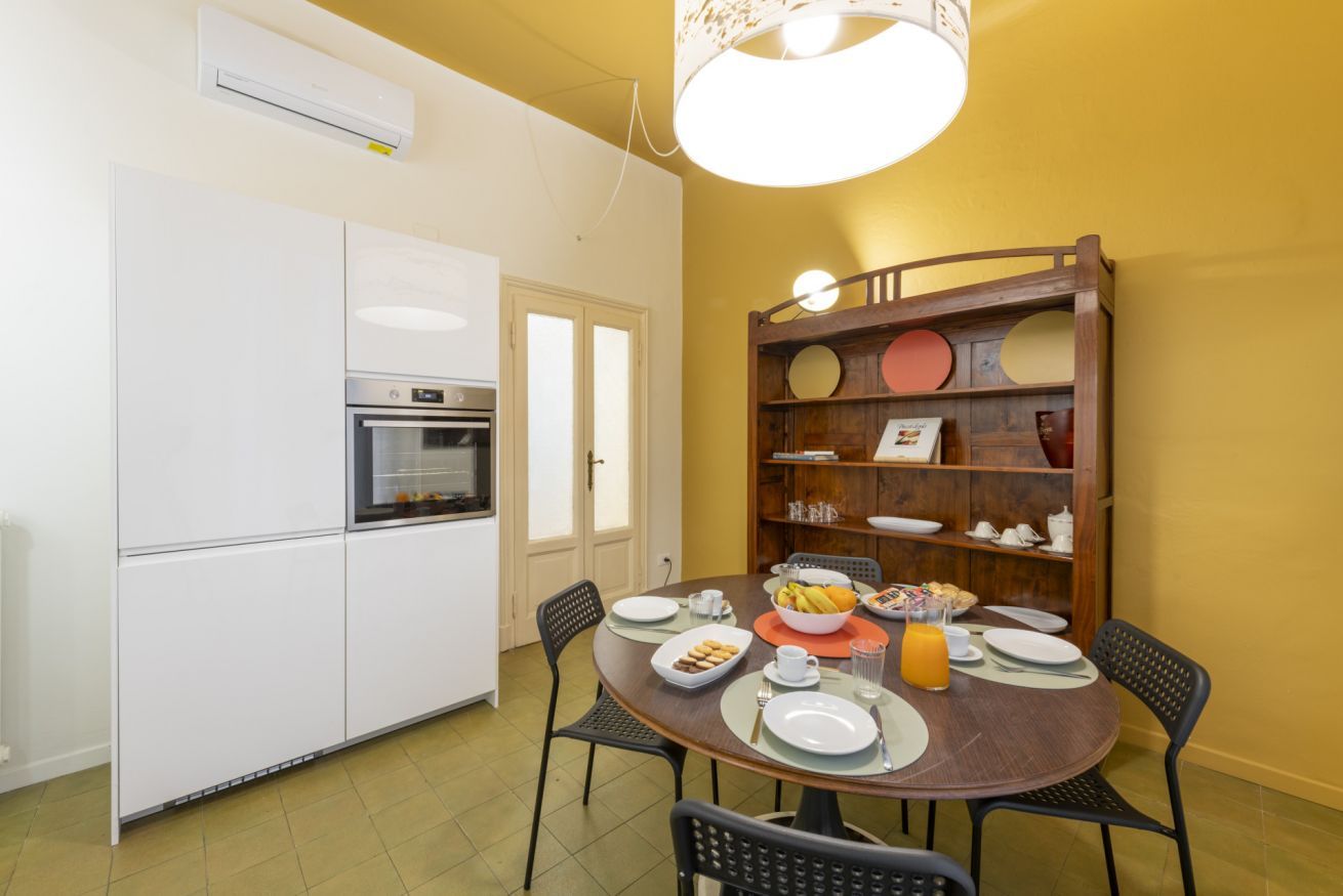Uma sala de jantar com mesa redonda, cadeiras, um aparador e uma cozinha com forno.