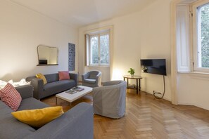 A living room with a sofa, armchair, coffee table, TV, and a window.