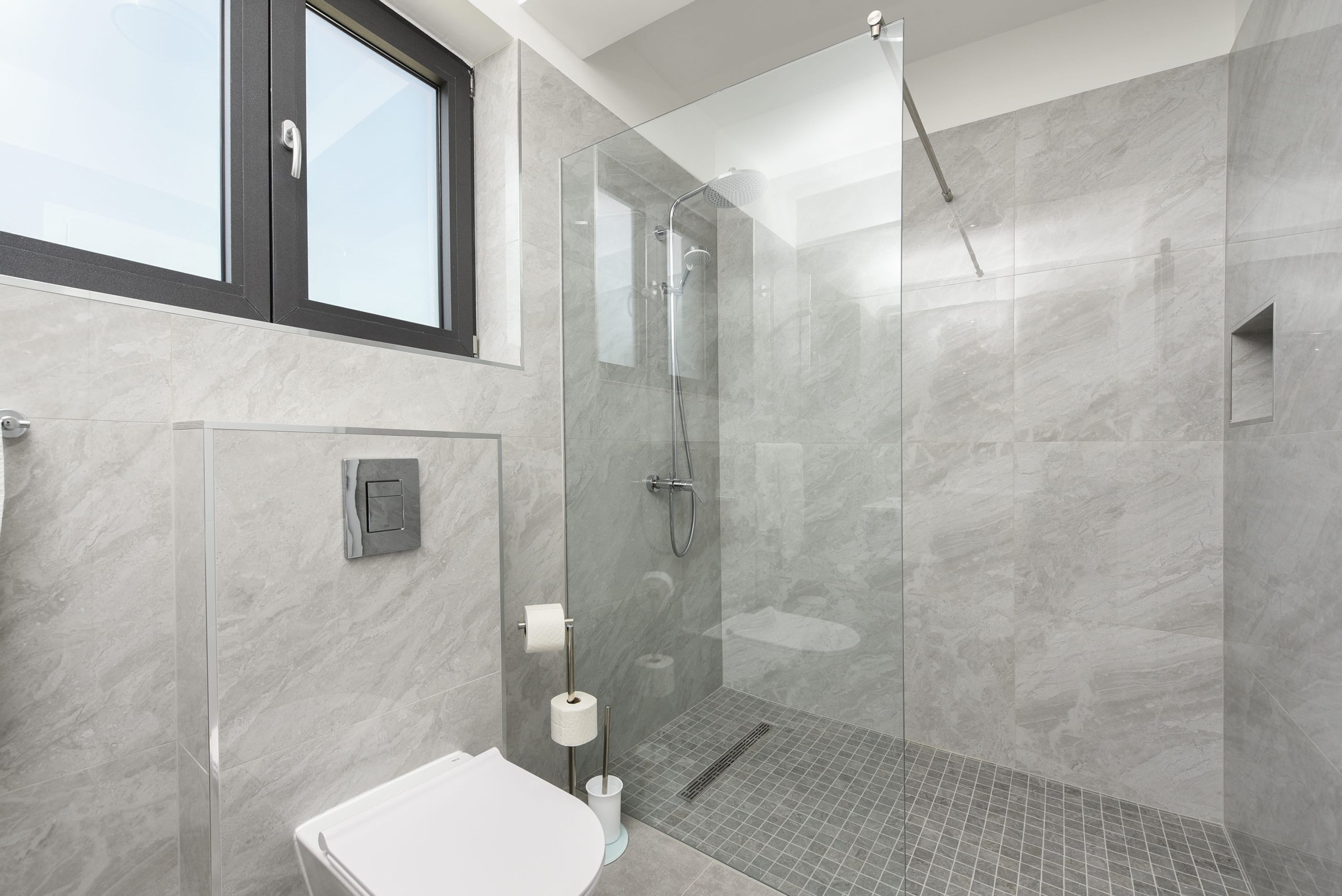 A modern bathroom with a glass-enclosed shower, a toilet, and a marble wall.