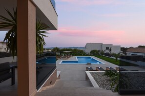 A rooftop pool area with two pools, lounge chairs, and a view of distant mountains.