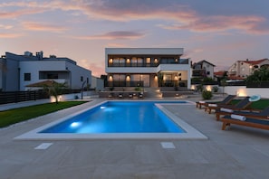A modern two-story house with a swimming pool and lounge chairs.