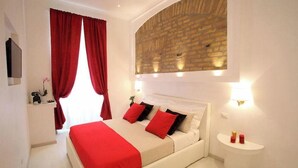 Un dormitorio con una cama grande, cortinas rojas, un detalle de pared de ladrillo y una mesita de noche pequeña con dos velas rojas.