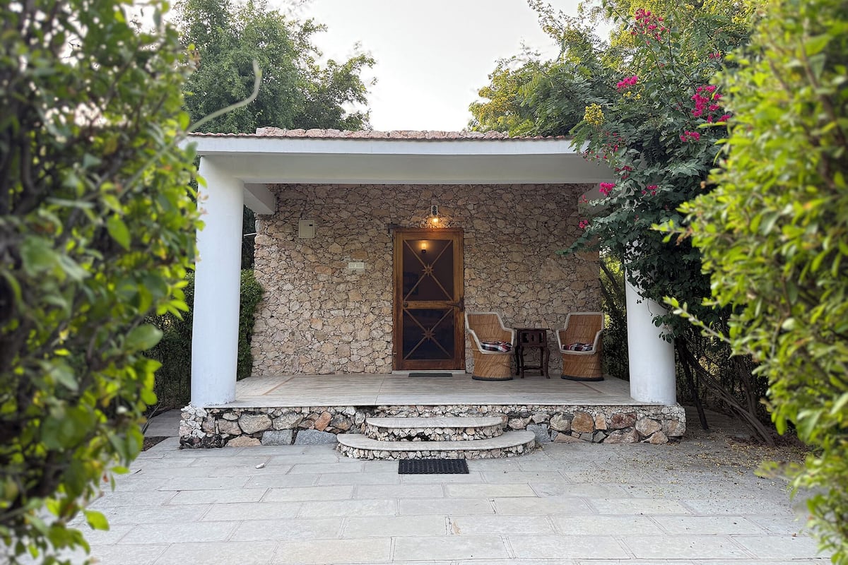 Un bâtiment aux murs de pierre, doté d’une porte en bois, de deux chaises en osier et d’une petite table sur un patio dallé de pierres.