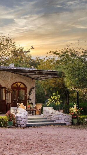 A stone house with a covered porch, a wooden door, and a small outdoor seating area with chairs and a table. - Korta Escape - A Heritage Resort (Sumerpur)