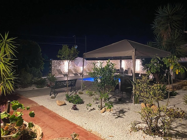 An outdoor patio area with a covered seating area, a pool, and various plants.