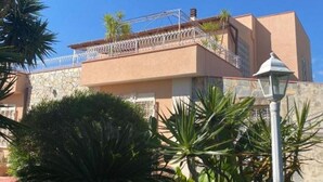 A modern building with a stone facade, a balcony with metal railings, and lush greenery around it. - Apartment 1-Villa Augusta del Sol (Fontane Bianche)